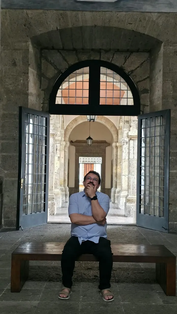 Padre Jocleilson diante do mural do presbitério, ao lado da cruz processional